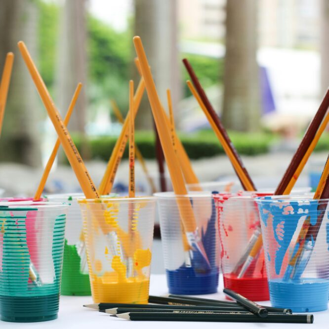 Vibrant paint brushes and pencils in plastic cups for arts and crafts.