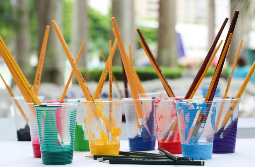 Vibrant paint brushes and pencils in plastic cups for arts and crafts.